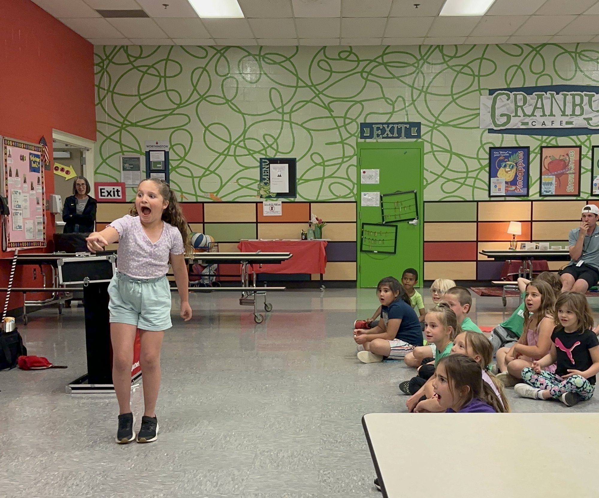 A girl standing in front of her whole school during a Carroll Baker assembly, caught mid-reaction